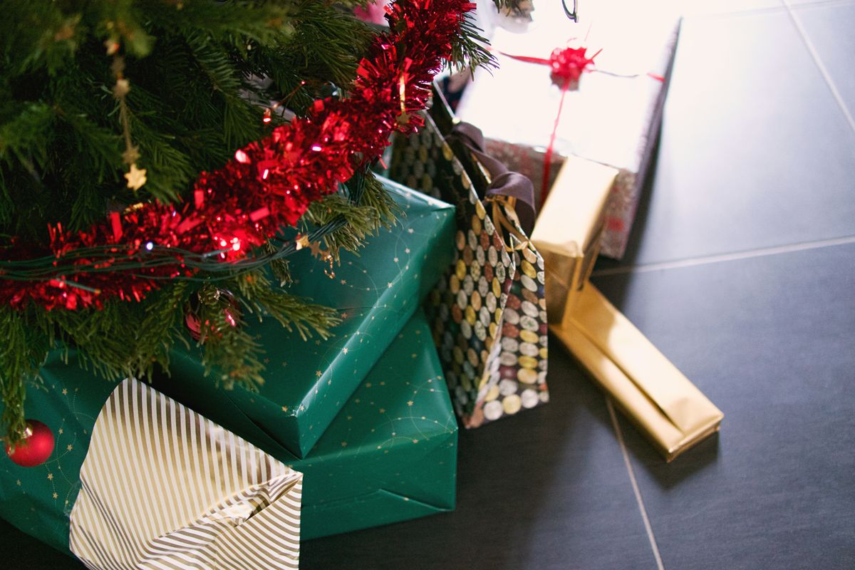 Colorful presents under a Christmas tree with red tinsel garland.